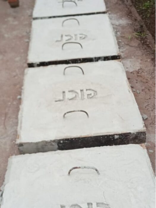 Row of precast concrete manhole cover slabs with metal lifting handles laid end to end on the ground